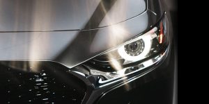 Close up view of the front driver side of a gray 2020 Mazda3 Sedan with the headlight brightly lit. | Mazda dealer in St. Louis, MO