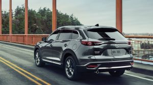 A charcoal 2020 Mazda CX-9 being driven over a bridge with a body of water and trees in the background. | Mazda dealer in St. Louis, MO