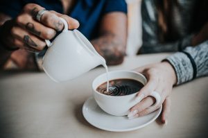 Close up of a man's hand pouring milk into cup of coffee with a woman's hand holding onto it. | St. Louis, MO