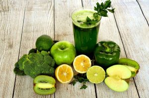 A dark green smoothie on a wooden table surrounded by a lemons, limes, an apple half, a kiwi half, a bell pepper, and a head of broccoli. | St. Louis, MO