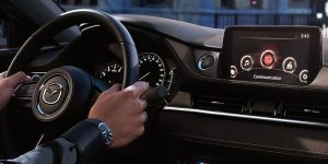 Interior view of the dashboard area with a a man holding the steering wheel of a 2020 Mazda6. | Mazda dealer in St. Louis, MO.