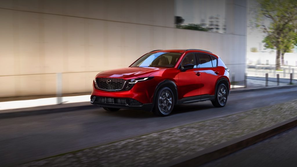 Red Mazda CX-5 driving on a city street with motion blur and reflections on the windows.